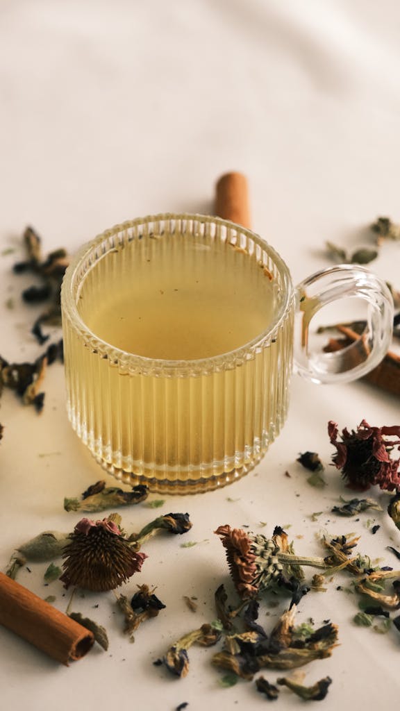 Glass cup of herbal tea surrounded by dried flowers and cinnamon sticks.